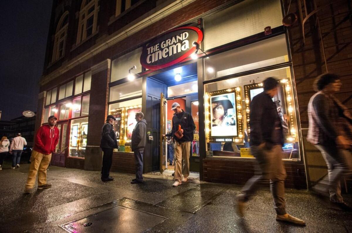 Patrons exit The Grand Cinema on a rainy evening. 