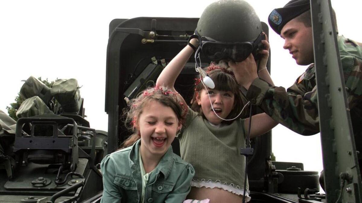Pfc. Ian Collins, right, helps Arianna Lammers, 10, center, try on a soldier’s helmet, while Madison Shifflett, 8, delights in checking out some of the Stryker Command Vehicle features during Armed Forces Day in 2006.