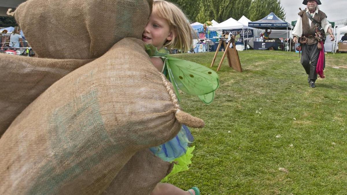 Three-year-old Lucy Clark of Tacoma carries bags of “coffee” and “sugar” in a pirate-run game of “Load th’ Cargo,” part of the Maritime Festival in 2012.