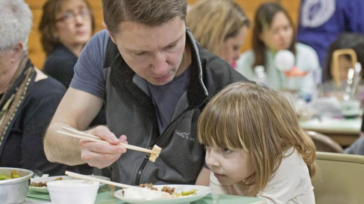 Gary Turner helps his daughter Grace Turner use chopsticks for the first time at a Tacoma Buddhist Temple fundraiser in 2012. The temple hosts fundraisers twice a year, in the spring and fall. The fall event, held Sunday this year, includes a bake sale and a menu of teriyaki, udon and unagi bowls, in addition to a craft and art sale.