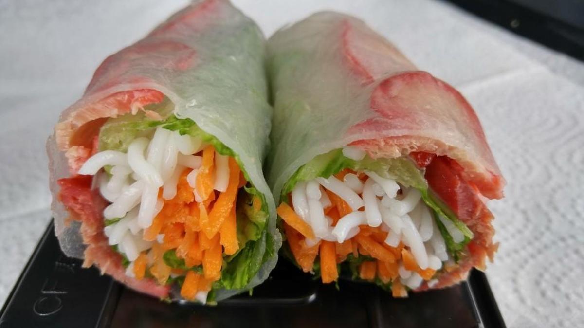 A barbecue pork fresh roll with noodles, chopped carrots, herbs and lettuce rolled up in a rice wrapper.