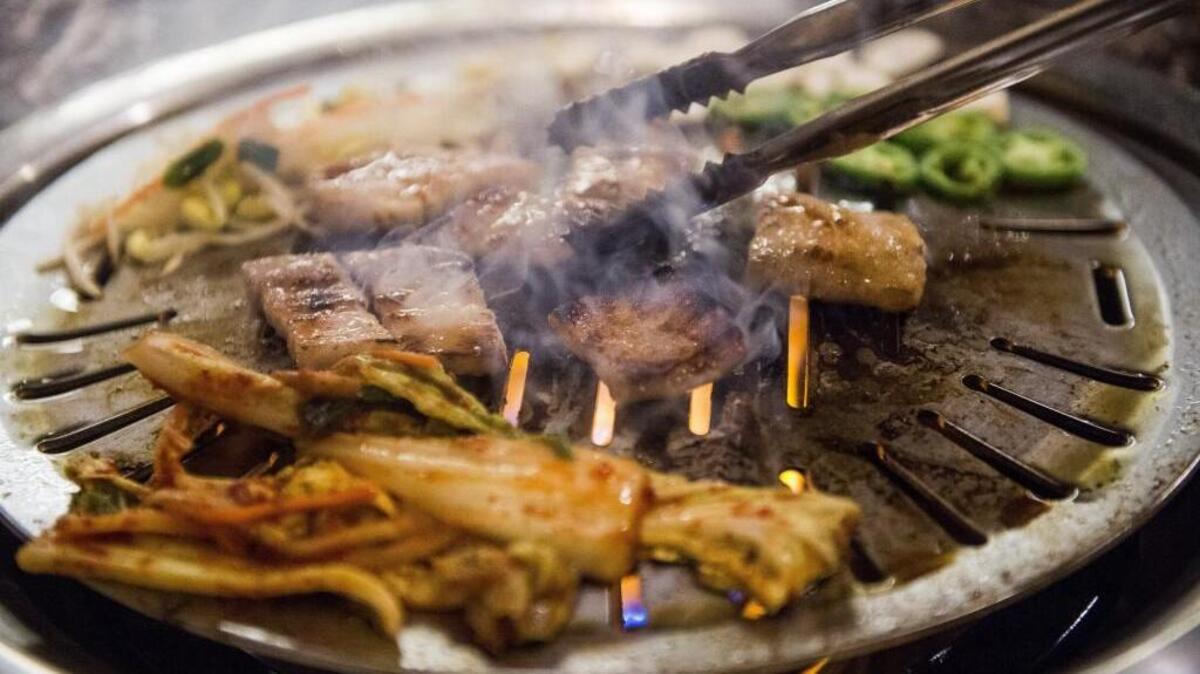 Thick-sliced pork belly, kimchi, and bean sprouts cook on a barbecue table at Dae Won Garden in Lakewood, Wash., on Monday, Nov. 13, 2017.