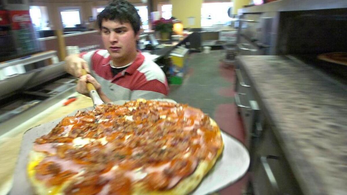 
Trackside Pizza employee Chris McMinn gets a three-meat pizza out of the pizza oven at Trackside Pizza in Puyallup. 
