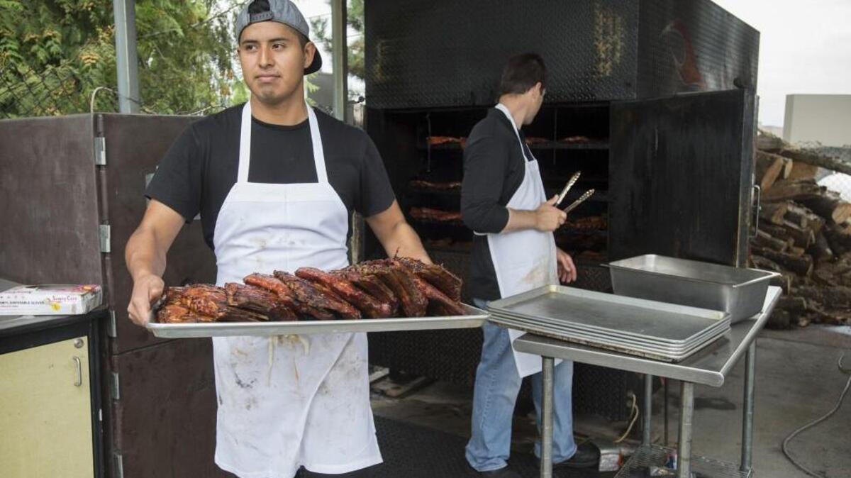 Luis Morales of Tacoma carries away a tray of spare ribs as co-owner Preston Brank pulls the finished product from the smoker at Brank’s BBQ in Sumner.