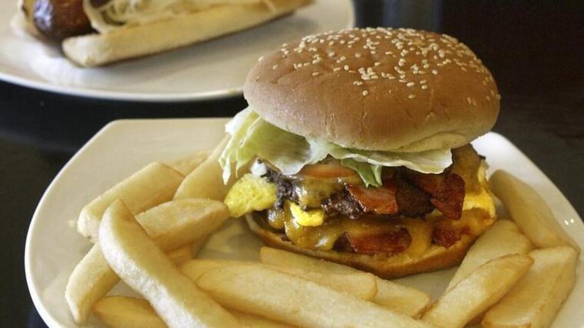 The classic Friesenburger is a half-pound double burger with bacon, egg and cheese served with a side of steak fries. In the background is a deep-fried hot dog with relish and sauerkraut.