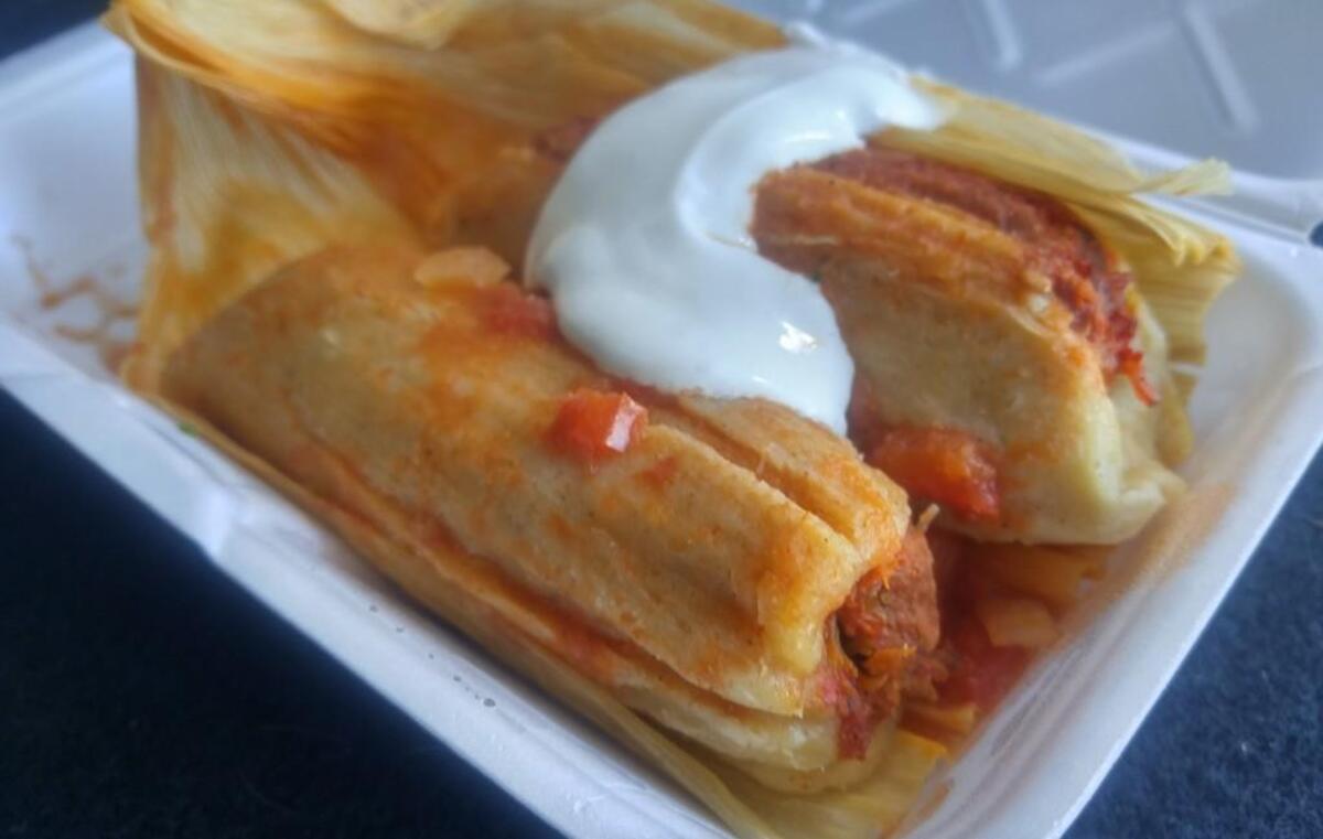 A pork tamale with red sauce and topped with sour cream.
