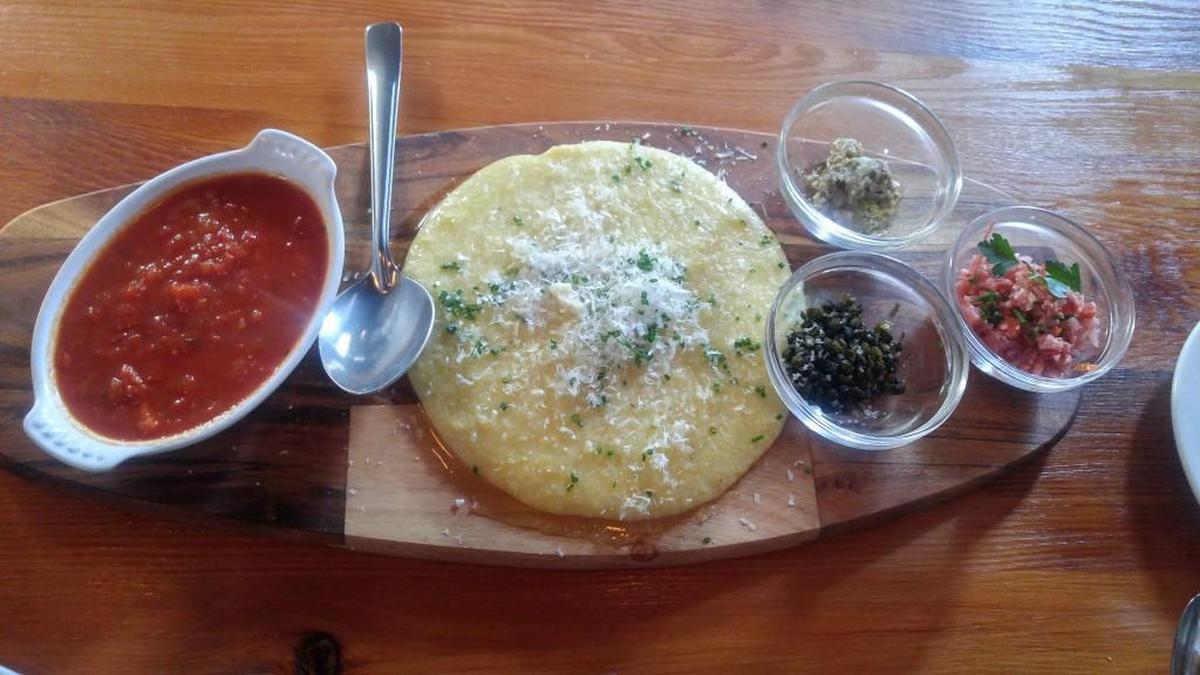 A plate of polenta flanked by add-ins from En Rama. The polenta is served on a wood board.