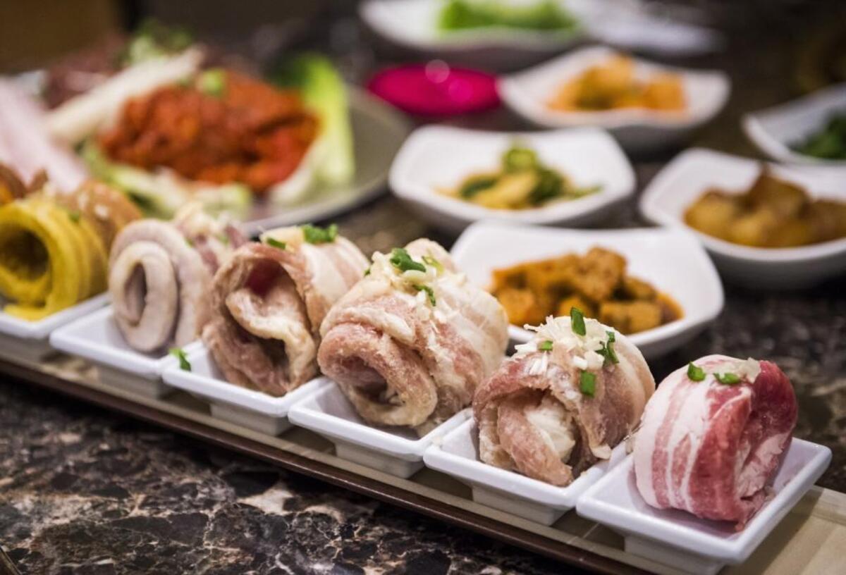 A tray of eight flavored pork-belly strips and a variety of banchan dishes are shown at Dae Won Garden in Lakewood, Wash., on Monday, Nov. 13, 2017.