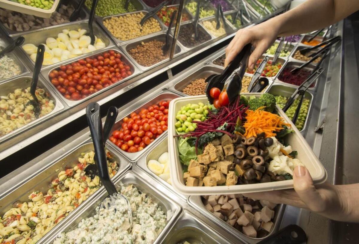 Some of the fresh, organic ingredients available at the salad bar at Marlene's Natural Foods Market in Tacoma. Besides the fresh vegetables being loaded on this customer's plate, there are prepared salads like the pea-and-cheese and Greek, top left.