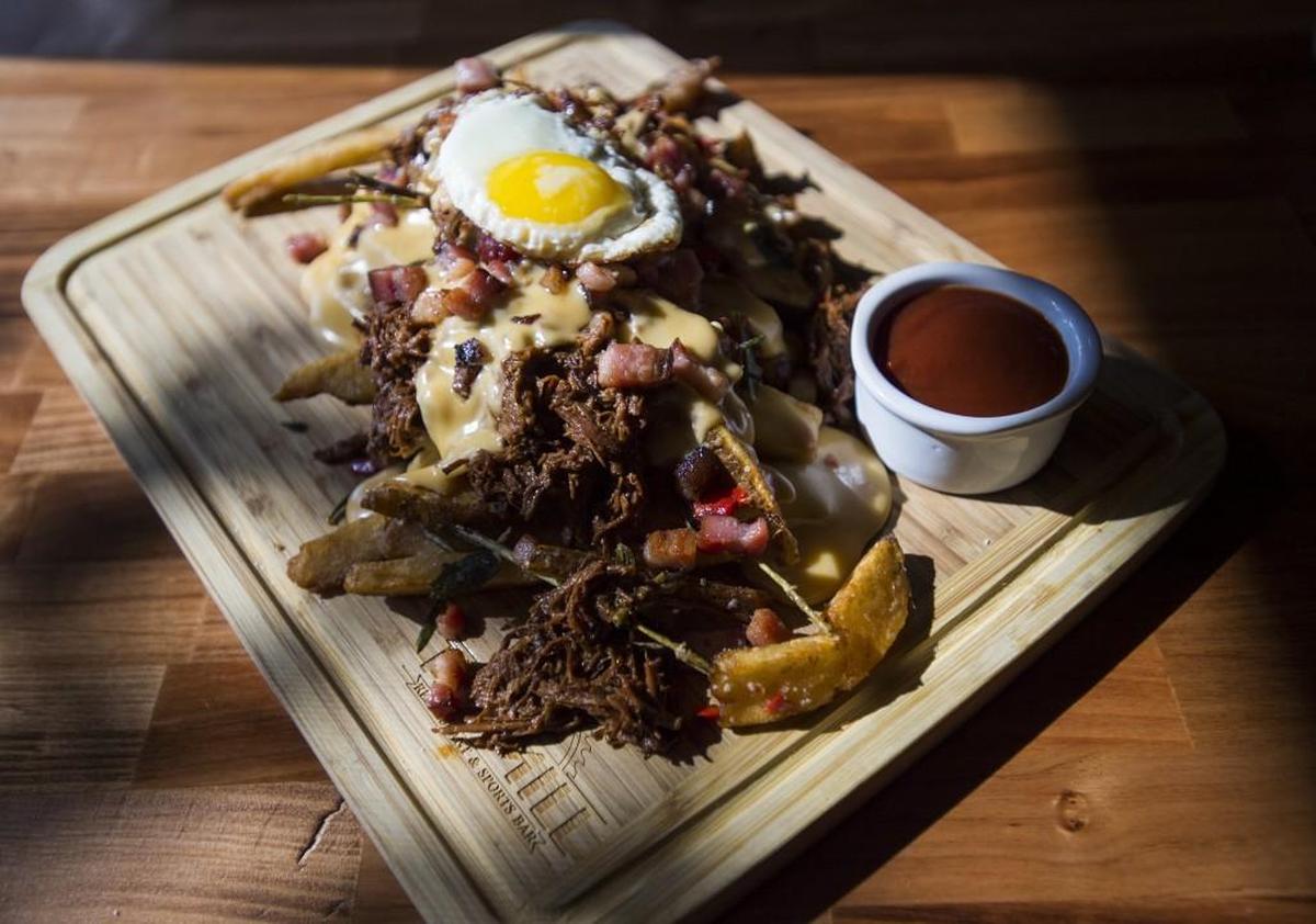 Filthy Pork Fries featuring handcut fries, pulled pork made from Kurobuta pork, beer cheese, fried Kurobuta pork belly and topped with a fried egg. Served at the Mill Restaurant and Sports Bar in Milton.