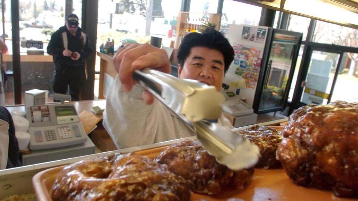 Pao Lo grabs some apple fritters off the tray in his business, Pao’s Donut & Coffee Shop