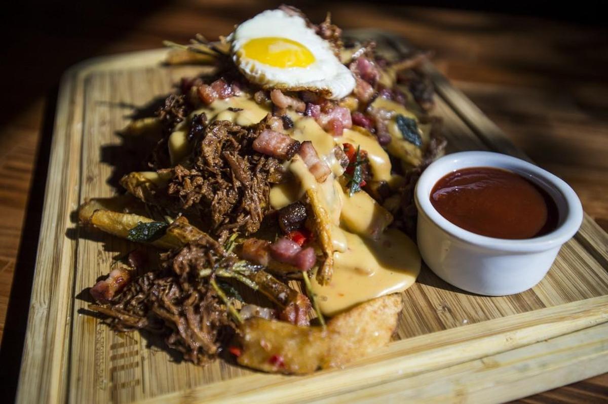 Filthy Pork Fries featuring hand-cut fries, pulled pork made from Kurobuta pork, beer cheese, fried Kurobuta pork belly and topped with a fried egg. Served at the Mill Restaurant and Sports Bar in Milton.