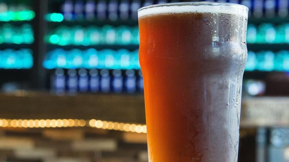 
A pint of Ottzel Quatzel sits on a table at Tacoma’s Odd Otter Brewing, with the bar’s glasses illuminated in their display behind the counter.
