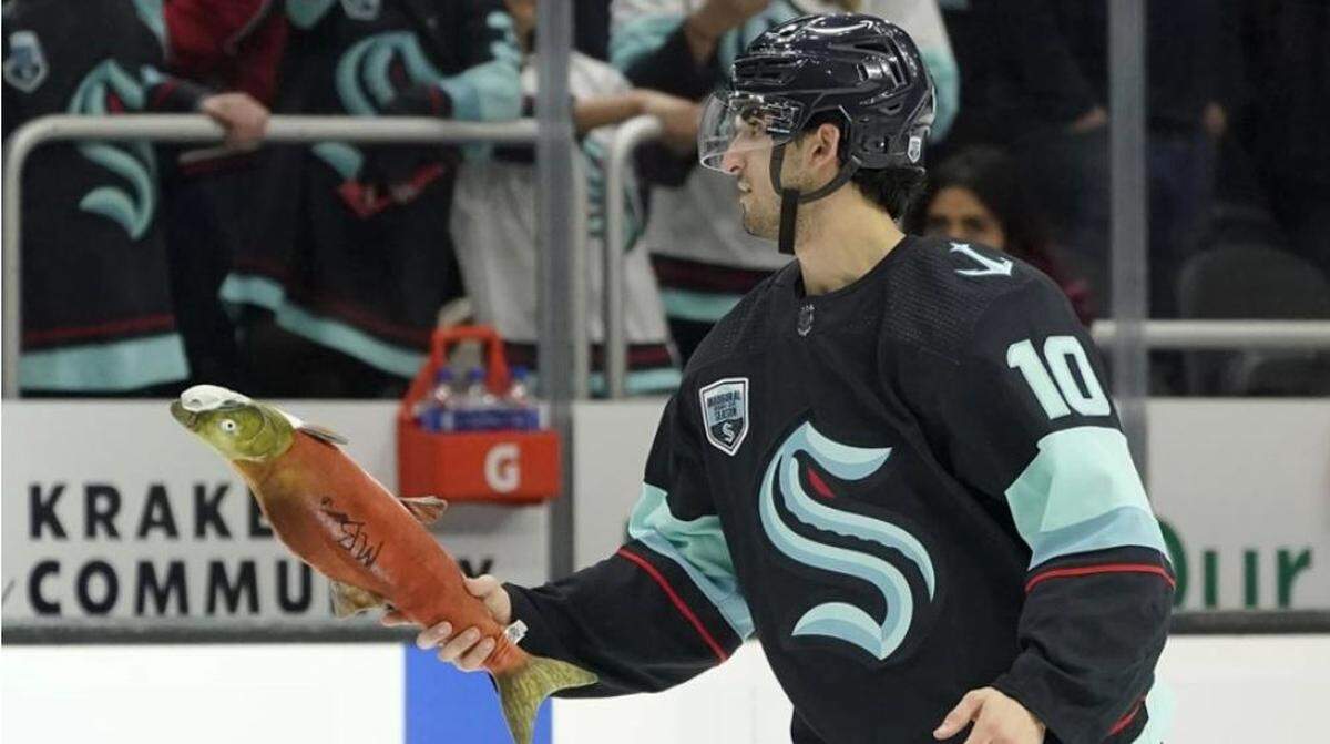 Matty Beniers after a Kraken home win. After Seattle wins, Kraken players voted the three stars for the game (by hockey tradition) grab fake salmon from team employees dressed like fishermen and women, autograph the salmon and throw the fish over the glass to screaming fans. It’s Pike Place Market at Climate Pledge Arena.