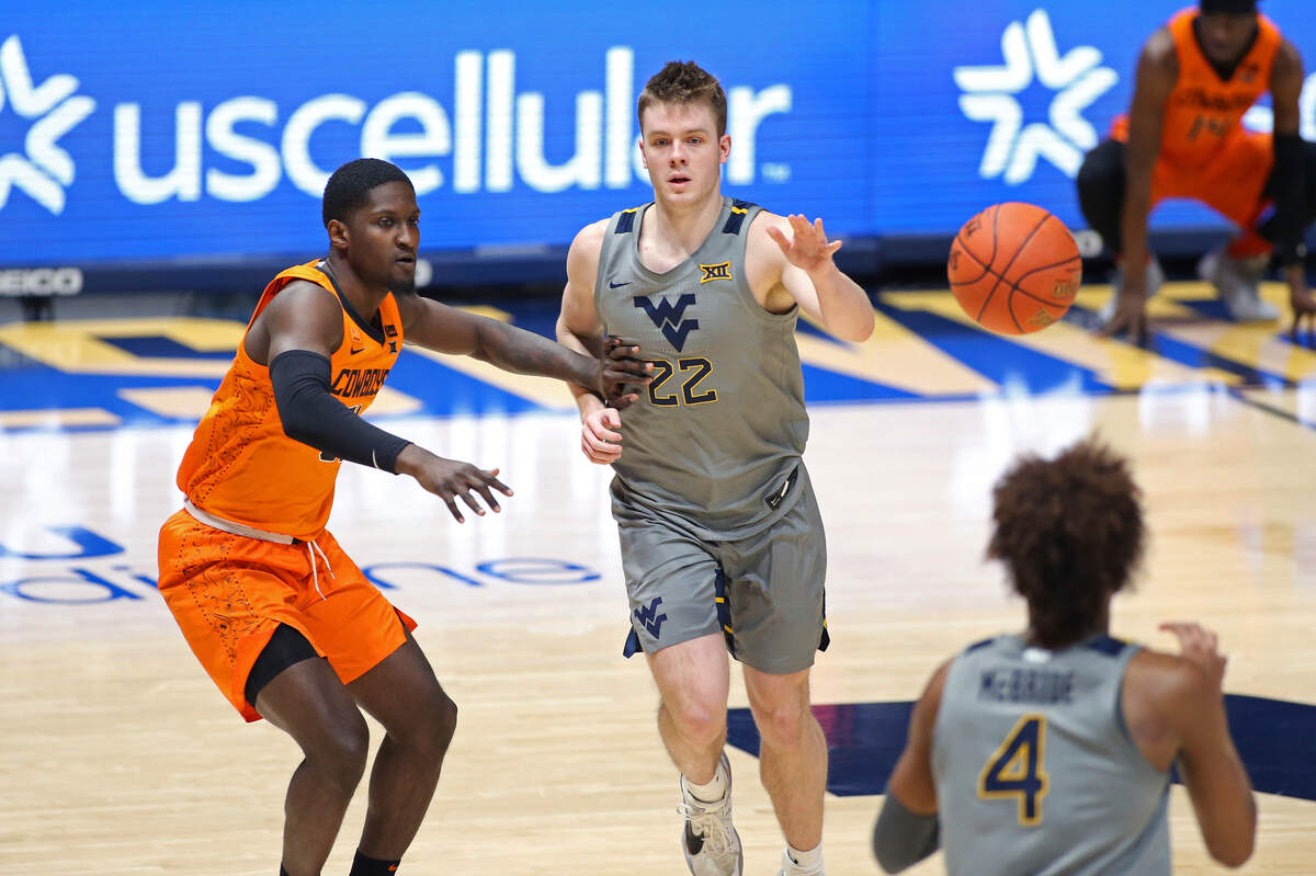 West Virginia guard Sean McNeil (22) passes to guard Miles McBride (4) while defended by Oklahoma State guard Ferron Flavors Jr. (31) during the second half of an NCAA college basketball game Saturday, March 6, 2021, in Morgantown, W.Va. (AP Photo/Kathleen Batten)