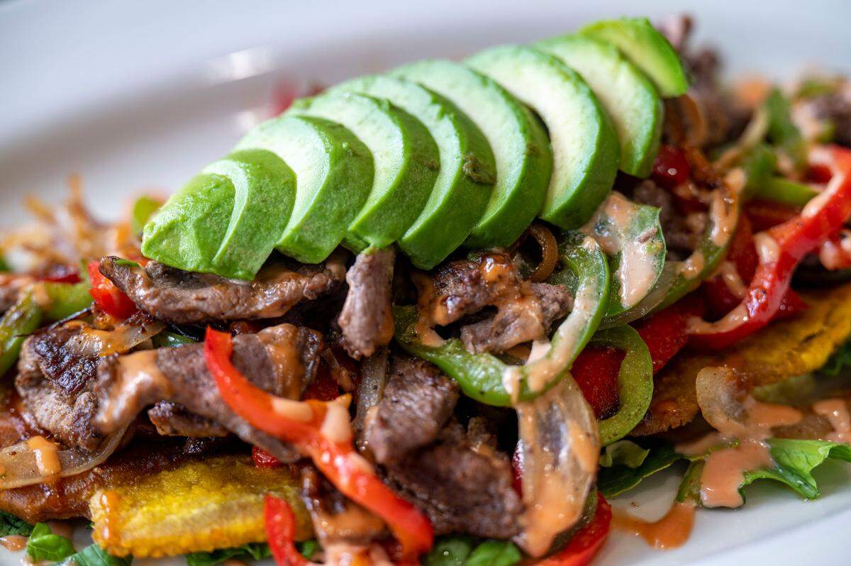 The steak patacone begins with a smashed, fried plantain that acts as a vehicle for carne asada, sauteed bell peppers, and avocado.