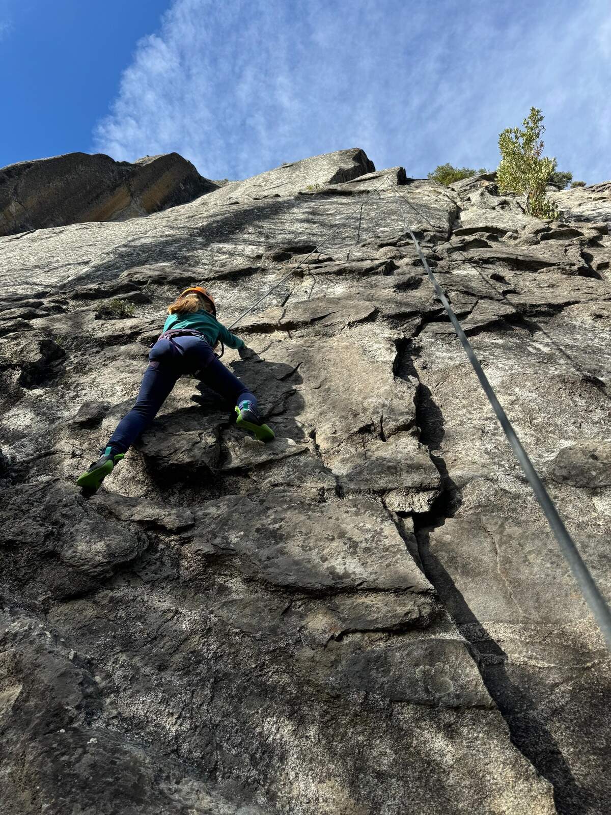 A young girl climbs on “top rope” using a fixed anchor above.