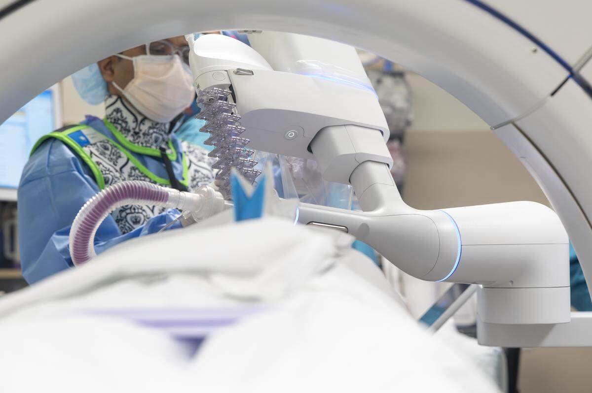 The arm of the DaVinci ION robotic surgery system is visible between the ring of an X-ray machine and Abhishek Biswas, left, a pulmonologist with Multicare Health, as he uses the ION for a lung biopsy procedure on Wednesday, May 21, 2025, at Good Samaritan Hospital in Puyallup, Wash.