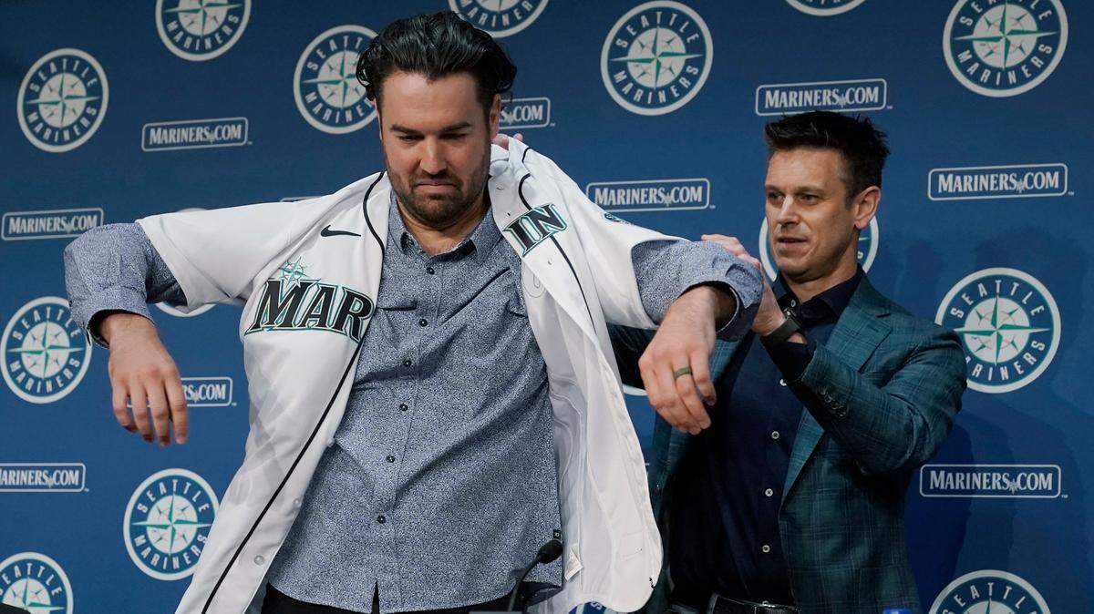 Jerry Dipoto, right, Seattle Mariners President of Baseball Operations, helps new Seattle Mariners pitcher Robbie Ray put on his jersey, Wednesday, Dec. 1, 2021, during a news conference in Seattle. The AL Cy Young Award winner — who previously pitched for the Toronto Blue Jays — signed a five-year contract with the Mariners. (AP Photo/Ted S. Warren)