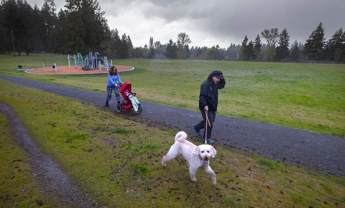 Alan Shelton walks his dog, Bentley, as his wife, Shari Shelton pushes their granddaughter, Raeyah, as they escape a rain shower after playing on the new jungle gym equipment at the Lidford Playfield in Waller, Washington, on Tuesday, April 26, 2022.