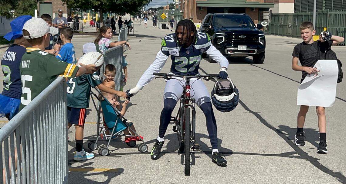 Cornerback Riq Woolen rides a Green Bay boy’s bike down the road from the Seahawks’ locker room at Lambeau Field to the fields across the street for Seattle’s NFL preseason joint practice with the Packers in Wisconsin Thursday, Aug. 21, 2025.