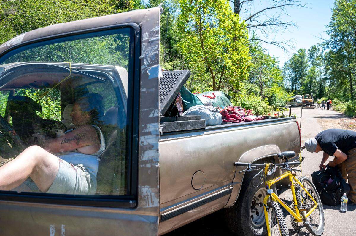 Two people living at the small homeless encampment near Cheney Stadium wait to have a pickup truck towed away from the area as crews from Metro Parks sweep up the area on Friday, June 24, 2022.