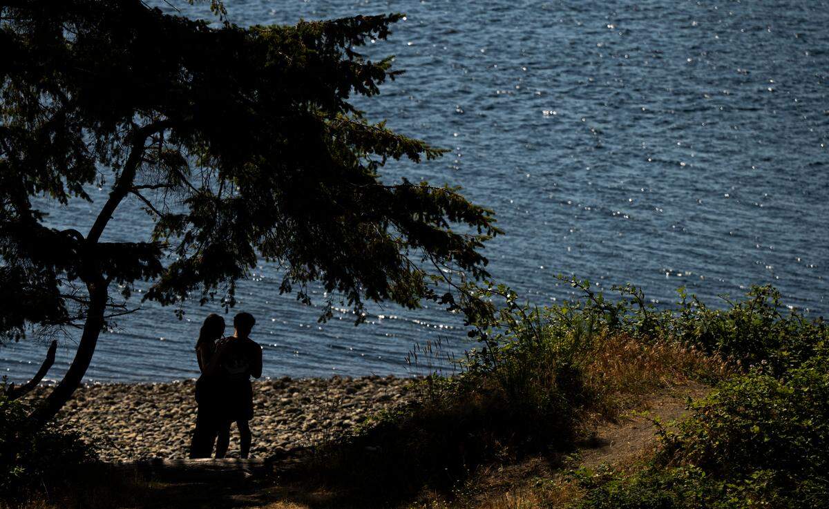 As temperatures reach the high 80s, a couple stands in the shade at Chambers Bay Beach on Monday, June 30, 2025, in University Place, Wash. 