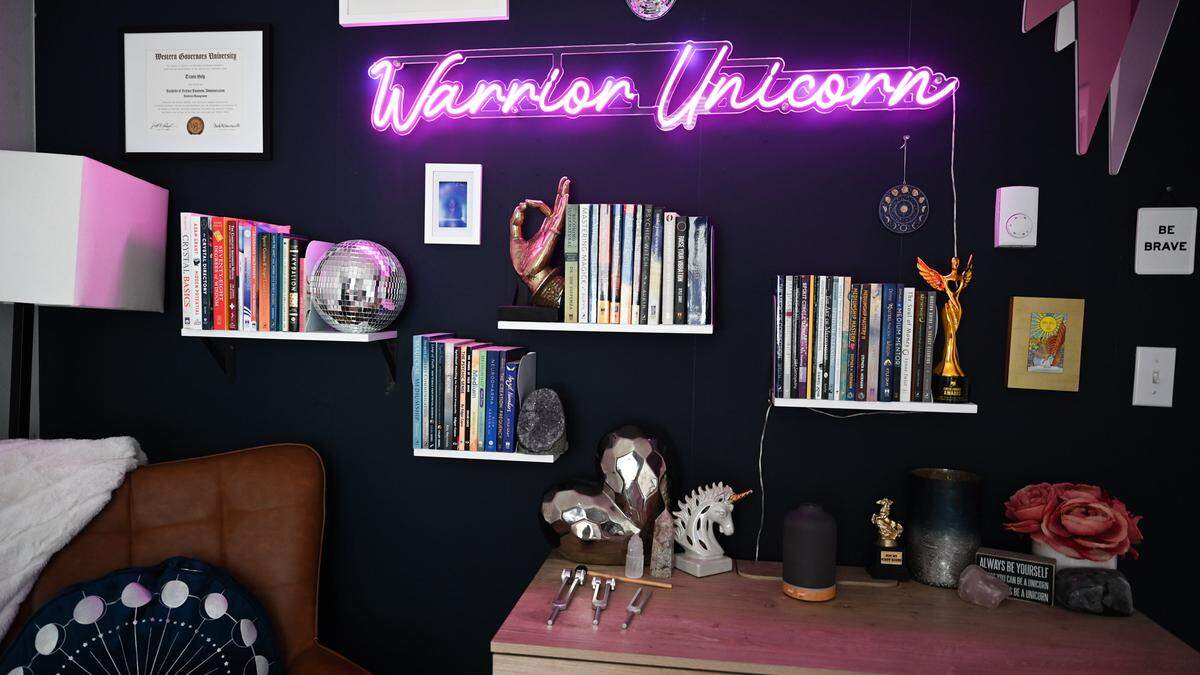 Books, photos, and a Neon light sign spelling out the nickname “warrior Unicorn, are a few thing lining the back wall of Travis Holp’s office on Friday, Aug. 9, 2024 in Tacoma, WA. Holp is a local psychic who became TikTok famous for his tarot readings.
