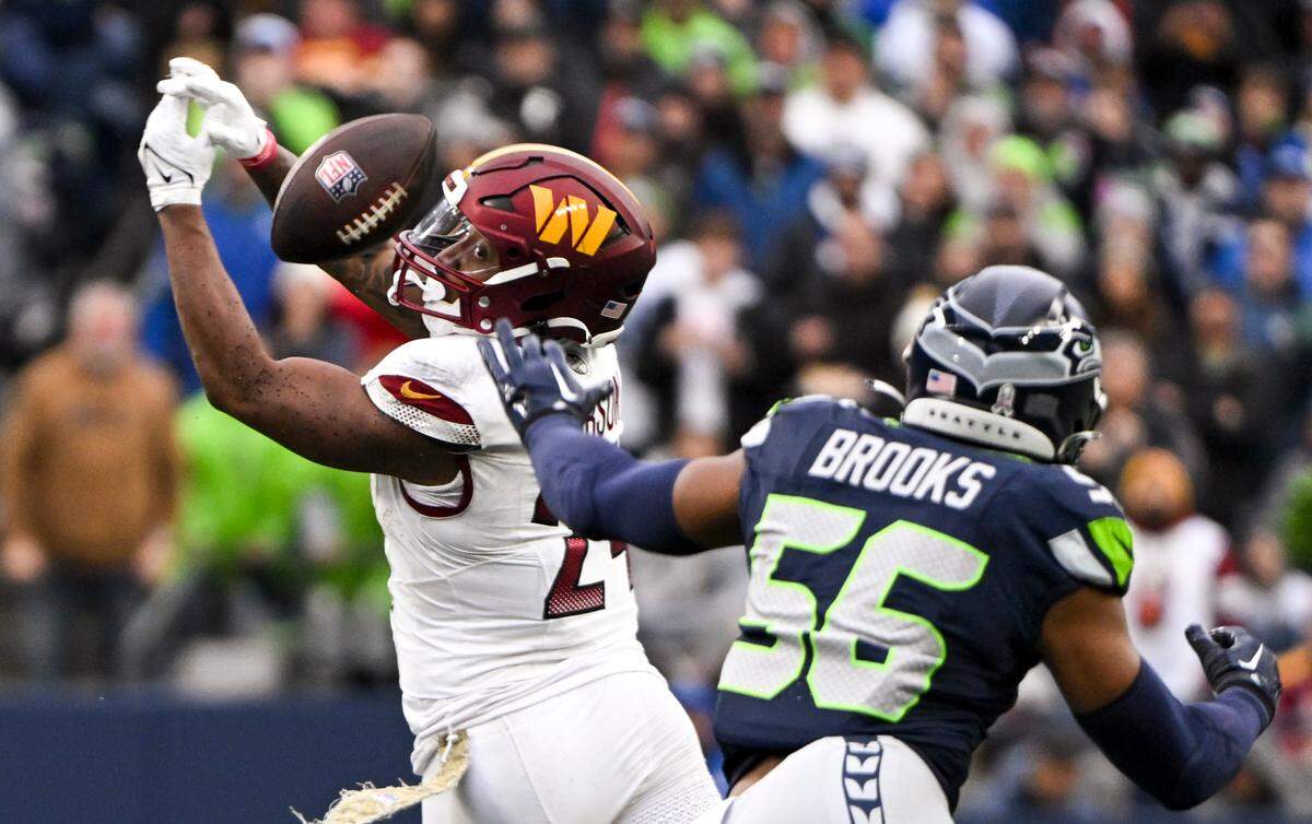 A pass goes through the hands of Washington Commanders running back Antonio Gibson (24) and nearly into the hands of Seattle Seahawks linebacker Jordyn Brooks (56) during the first quarter of the game at Lumen Field, on Sunday, Nov. 12, 2023, in Seattle, Wash.