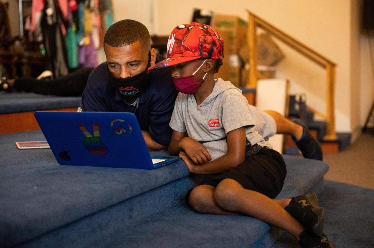 Turner Cagle, left, helps Nyrell McHenry login to his online schoolwork at the Multicultural Child and Family Hope Center community hall building in Tacoma, Wash., on Monday, Sept. 14, 2020.