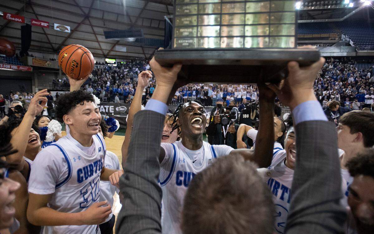 Curtis players Devin Whitten (from left), Zoom Diallo and Cinque Maxwell celebrate as head coach Tim Kelly hoists the state championship trophy folling the Vikings’ 52-49 overtime victory over Mount Si in the WIAA 4A Boys Basketball State Championship game in the Tacoma Dome in Tacoma, Washington, on Saturday, March 5, 2022.