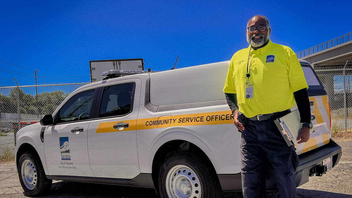 A community service officer, part of the Tacoma Police Department’s new program, stands in front of his vehicle.