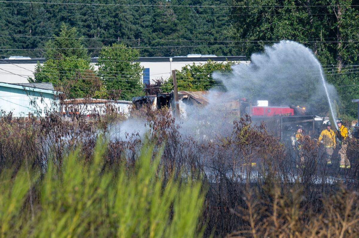 Firefighters from West Pierce Fire and Rescue water down hotspots in a field along the 7100 block of 146th Street SW in Lakewood, Wash., on Friday, Aug. 4, 2023. The brushfire caused multiple homes to burn down in the Jamestown Estates mobile home park adjacent to the field.