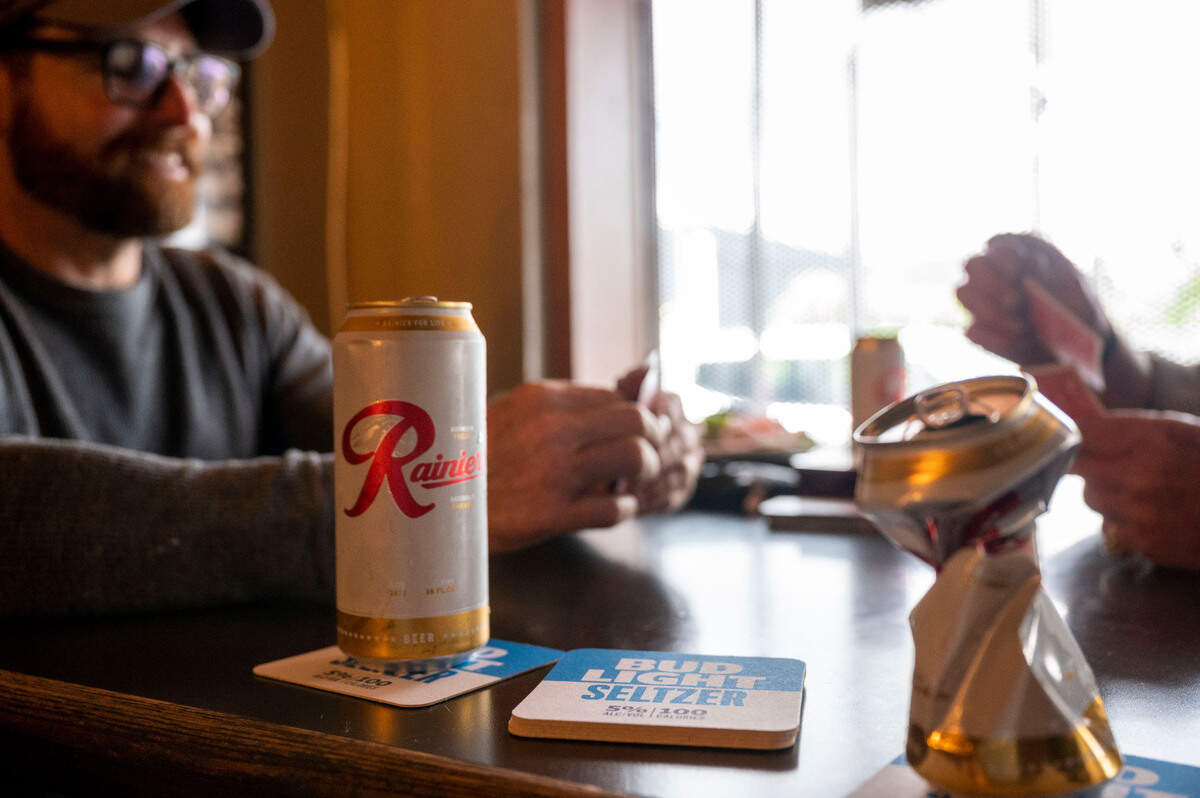 A full can and an empty can of Rainier sits at the table as Michael Holmes (left), of Tacoma, plays cribbage with Scott Raley, of Steilacoom, as they wait for their lunch at the Top of Tacoma Bar and Cafe on Friday, May 27, 2022, in Tacoma, Wash.