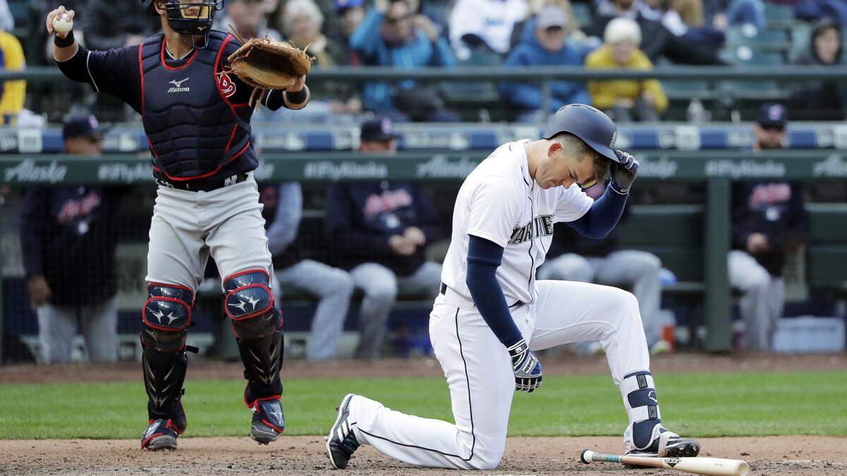 Seattle Mariners' Ryon Healy, right, kneels as Cleveland Indians catcher Yan Gomes, left, returns the ball after striking out swinging with two men on base to end the eighth inning of a baseball game, Saturday, March 31, 2018, in Seattle. (AP Photo/Ted S. Warren)