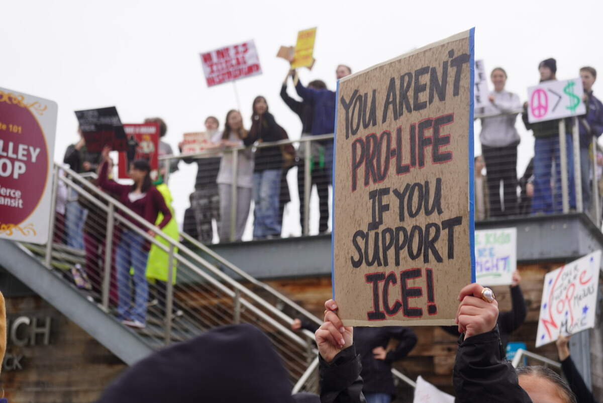 Protesters hold up signs near Skansie Brothers Park in Gig Harbor, Wash., during a walkout organized by Gig Harbor High School students to protest federal immigration enforcement, Friday, Feb. 13, 2026.