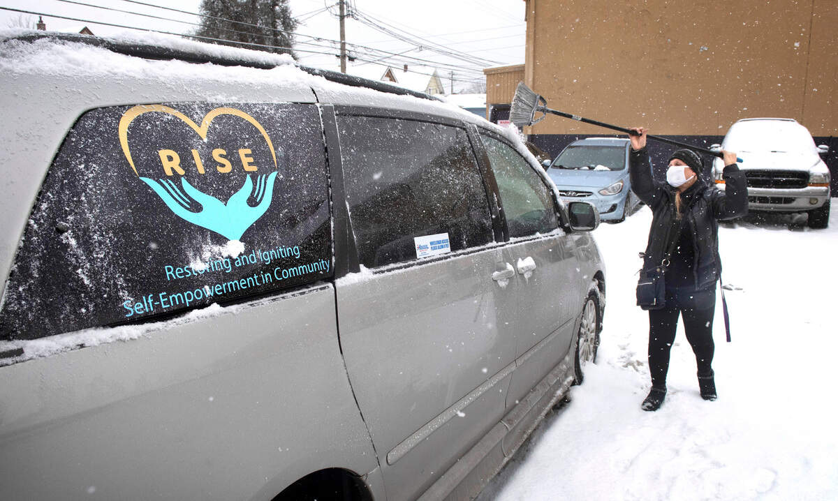 Outreach case navigator Traci Abbott clears snow off the RISE outreach van outside the warming center in Tacoma, Washington, on Tuesday, Dec. 28, 2021.