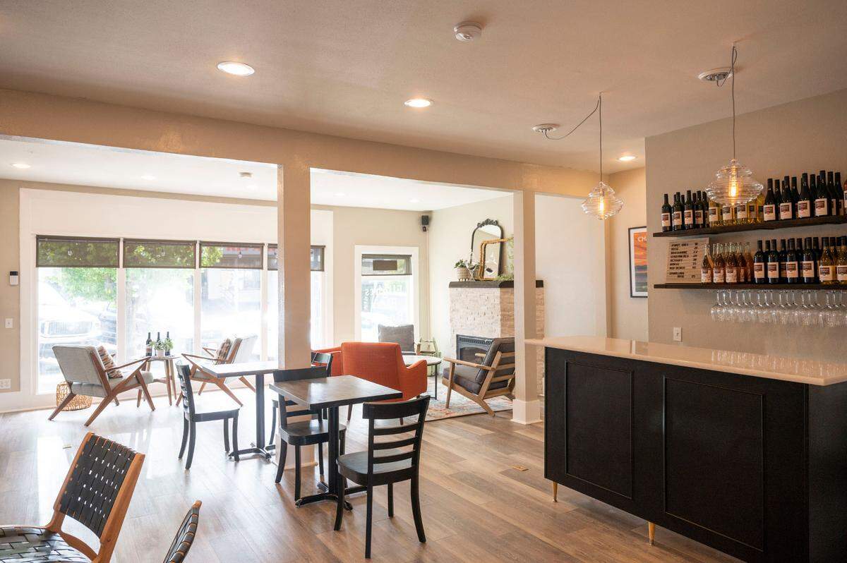 Dahlman Cellars tasting room in Tacoma features a small pour bar and four seating areas, including the Living Room with a couch and coffee table and the Fireplace Room with four lounge chairs.