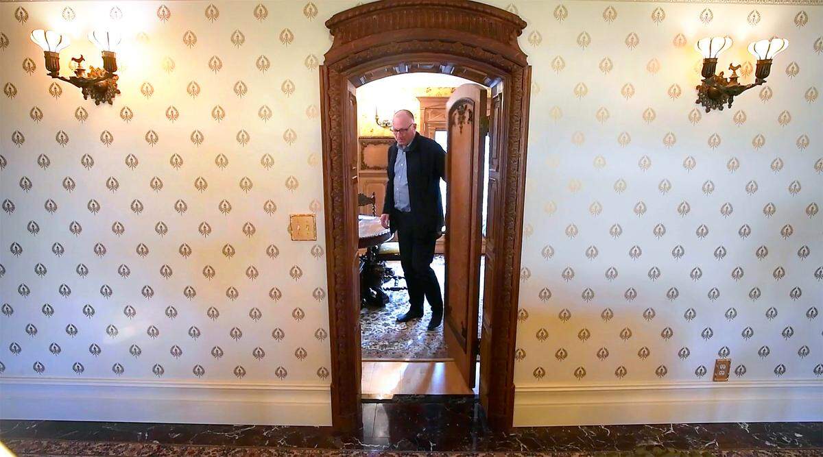 Realtor Mike Larson walks through 17th-century hand-carved doorway at the Thornewood Carriage House in Lakewood, Washington, on Tuesday, April 19, 2022. The home also features custom-designed wallpaper and electrically-repurposed gas lamps.