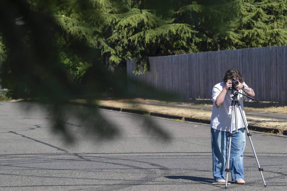 Easton Umansky uses a tripod to take photos of tree coverage in a neighborhood near Optimist Park on Tuesday, July 15, 2025, in the West End of Tacoma, Wash. These photographs are part of Umansky’s research project as a student at the University of Puget Sound.