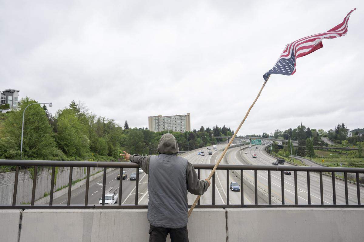 Shaun Anderson holds out a piece sign and waves an upside down American flag from an overpass above Interstate 5 on Wednesday, May 6, 2026, in Tacoma, Wash.