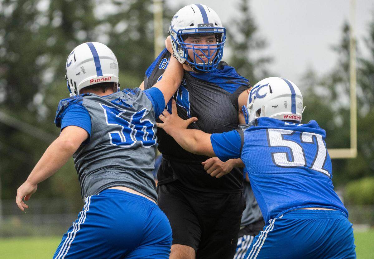 Eatonville Cruisers offensive lineman Tristan Lewis (64) is shoved by defensive lineman Nick Shipman (56) and linebacker Joel Thormodsgard (52) while running a play during practice at Eatonville High School in Eatonville Wash. on August 20, 2022.