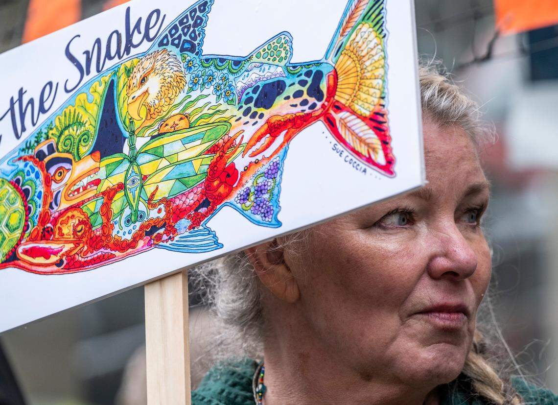 Sue Coccia holds a sign the she designed as she marches through downtown Tacoma to advocate for the removal of the Snake River dams and rally against the extinction of protected salmon in March 2022.