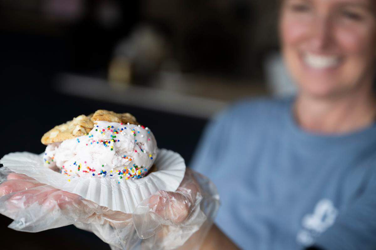 Owner Heidi Kenny holds out the Swiftie Sandwich, a scoop of honey lavender ice cream between two salted caramel cookies at Lick Homemade Ice cream, on Thursday, April 11, 2024, in Puyallup, Wash.