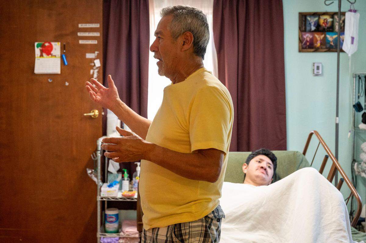 Armando Aragon stands in front of Brian’s bed explaining what he has done to remodel their mobile home to make it ADA accessible for his son. Armando and his wife, Maria Gonzalez, will be forced out of their home and will likely have to take Brian to a clinic, unless they can find a new place that would be accessible for their son.