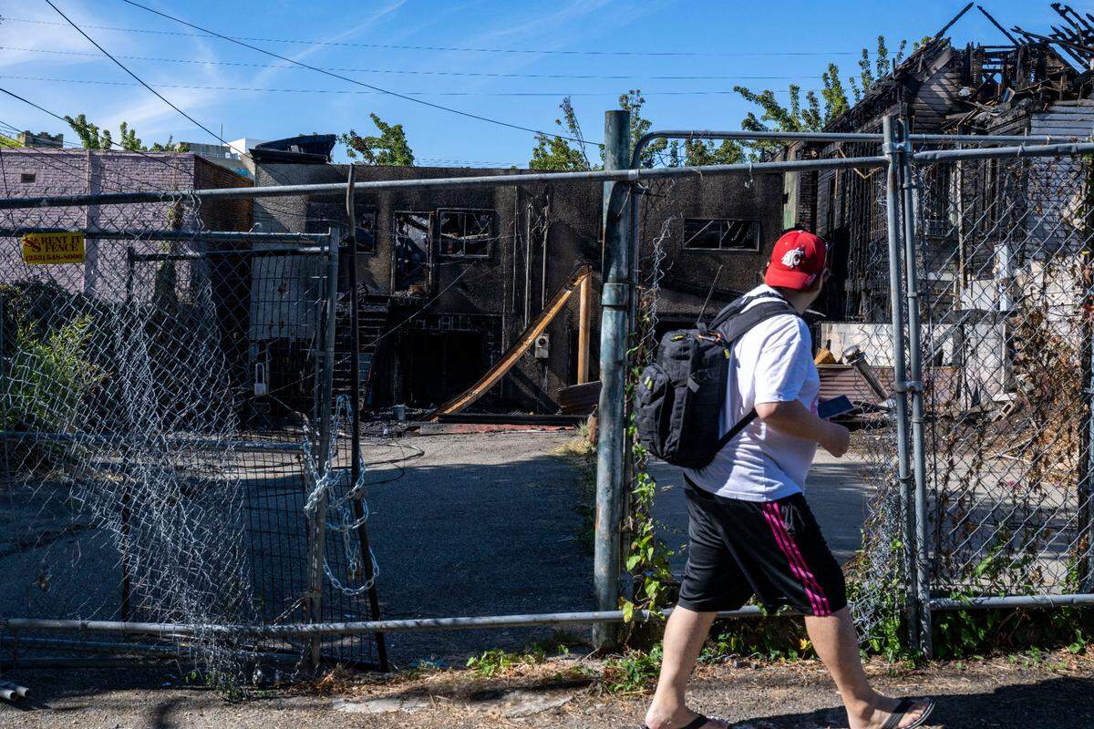 A man walks in the alley behind buildings that caught fire on Thursday night in the Stadium District on Friday, Aug. 4, 2023, in Tacoma.
