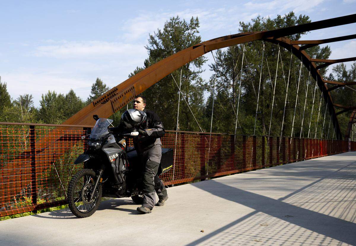 Connor Plett pushes his motorcycle  across the Foothills Trail Bridge as the White River Bridge remains closed on Wednesday, Aug. 27, 2025, in Buckley, Wash. The Foothills Bridge over the White River is the only thing connecting the towns of Buckley and Enumclaw.
