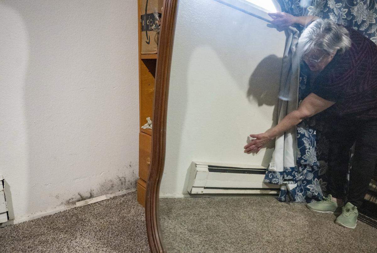 Lorine Rhodes, a resident at Westside Estates, pushes against a wall she says has been softened from flooding on Wednesday, May 13, 2026, in Tacoma, Wash. Mold, also from the flooding, is visible along the base of the wall.