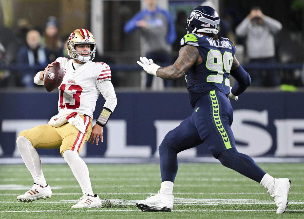 San Francisco 49ers quarterback Brock Purdy (13) scrambles under pressure from Seattle Seahawks defensive end Leonard Williams (99) during the third quarter of the NFC Divisional Round game at Lumen Field, on Saturday, Jan. 17, 2026, in Seattle.