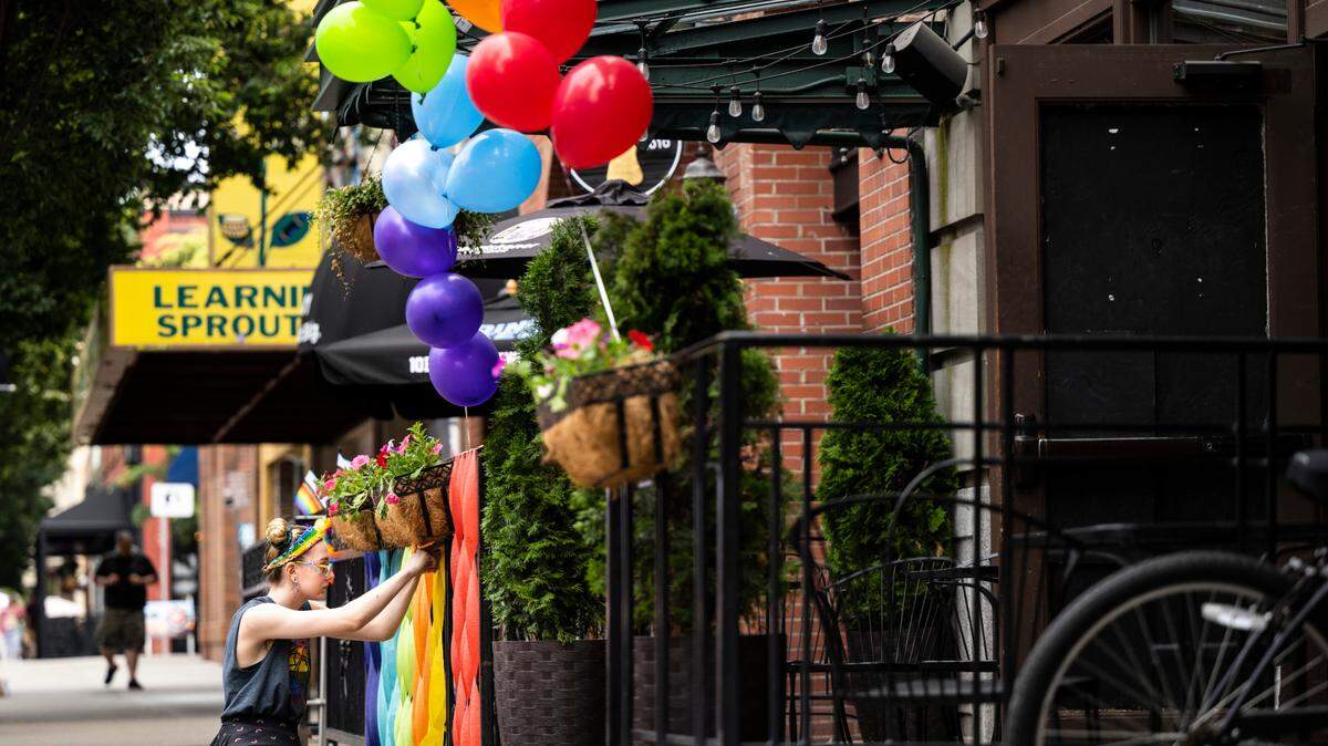 Eli Park decorates a fence outside of The Forum with colorful ribbons before the start of the Tacoma Pride Festival on Pacific Avenue in Tacoma, Wash. on Saturday, July 9, 2022.
